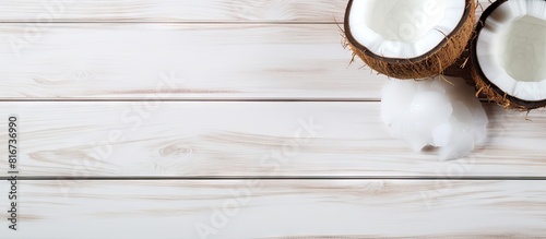 A tropical themed copy space image featuring a coconut on a white wooden background The coconut is half broken with its pulp exposed offering a view of its coconut water milk and oil The image is tak