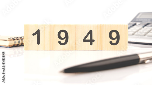 The numbers 1949 written on wooden cubes in a composition with a calculator, a pen on a white background