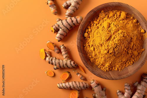 Top view of raw turmeric roots and ground curcuma powder in a wooden bowl isolated on a vivid orange backdrop
