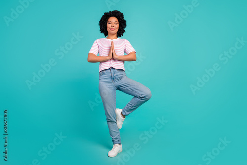 Photo of dreaming girl in pink t shirt and jeans stylish garment stand one leg meditation pose isolated on cyan color background