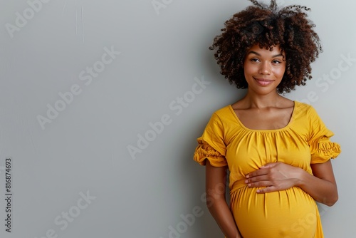 Pregnant African American woman tenderly hugging her belly on a gray background. The concept of preparing women for pregnancy, childbirth, motherhood.