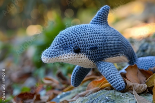 Charming crochet dolphin plushie sits amidst autumn leaves, evoking a playful contrast with nature