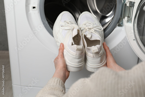 Woman putting stylish sneakers into washing machine, closeup