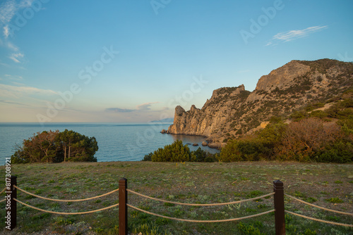 A beautiful view of the ocean with a rocky cliff in the background. The sky is clear and the sun is setting.