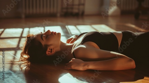 Under striking lighting, a graceful ballerina in a black outfit lies on the dance studio floor, her eyes closed.