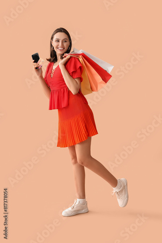 Young woman with credit card, mobile phone and shopping bags on beige background