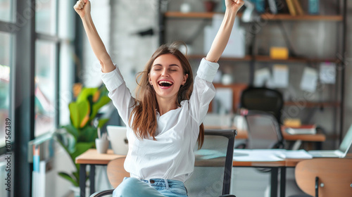 Startup young woman very happy and excited doing winner gesture with arms raised sitting on chair in office. 