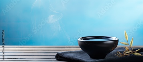 A copy space image featuring a spa concept background with water in a black bowl incense and a white towel placed on a blue wooden table