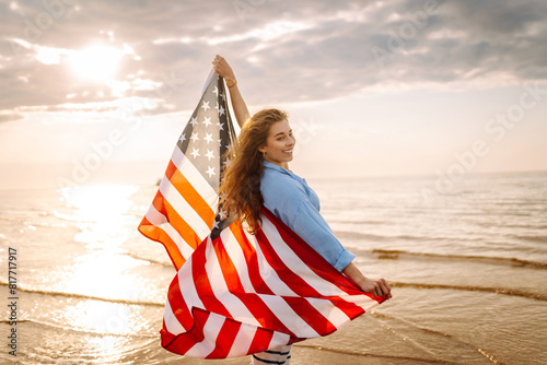 Young woman holding national American flag cover ocean beach holiday travel at summer romantic sunset. America independence day concept. 4th of July.