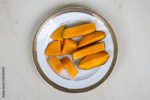 Ripe mango slices on a white plate on wooden background. Top view. 