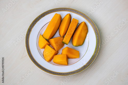 Ripe mango slices on a white plate on wooden background. 