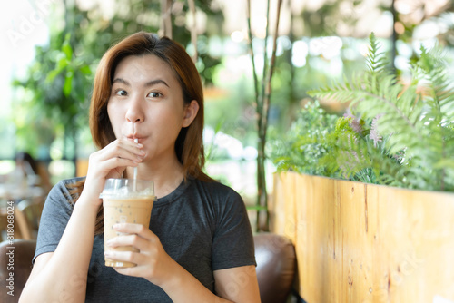 Asian woman drinking iced coffee in a cafe and smiling happily with the strong coffee taste.