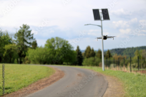 Dron w locie, w powietrzu, w tle panele słoneczne z latarnią uliczną.