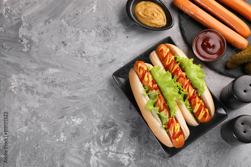 Tasty hot dogs and ingredients on grey textured table, flat lay. Space for text
