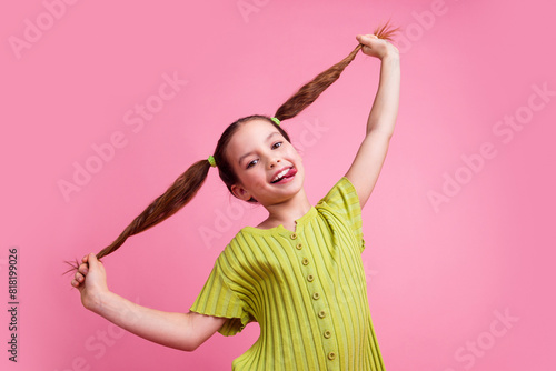 Photo portrait of cute little girl pulling tails stick tongue dressed stylish green clothes isolated on pink color background