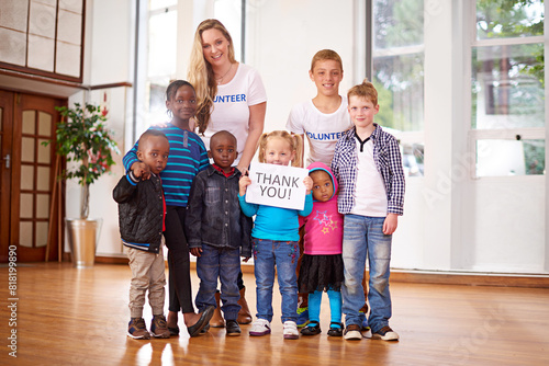 Children, volunteer and portrait at orphanage for donation, help and thank you sign for community service. Charity, kids and happy group with woman together at non profit ngo for support or gratitude