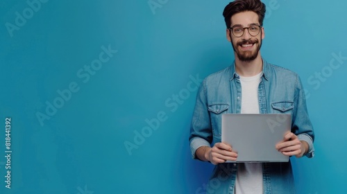 Photo of handsome smiling man holding laptop isolated on blue color background, eyes clearly visible and skin texture clean