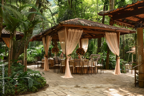A beautiful outdoor setting with a canopy and tables for a wedding reception. The tables are set with white tablecloths and chairs, and there are flowers and candles on the tables