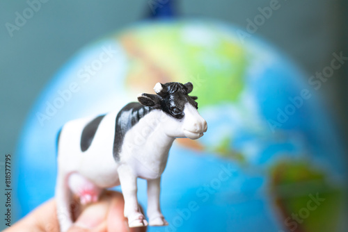 Plastic toy cow in front of world model background. Cows breeding and CO2 emission idea concept. Animal