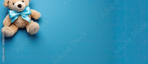 A teddy bear with a bow is seen from a top down perspective on a blue background providing ample space for an image