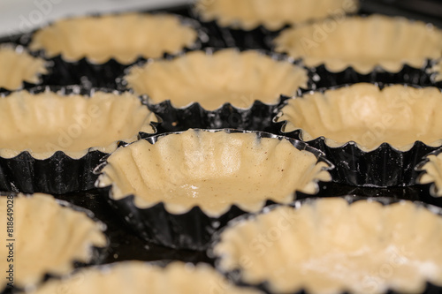Metalowe foremki na tartaletki wyłożone surowym kruchym ciastem przed pieczeniem 
