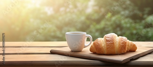 A coffee cup and a buttered fresh French croissant are placed on a wooden crate creating a food and breakfast concept A white board nearby displays the morning message have a nice day offering a visu