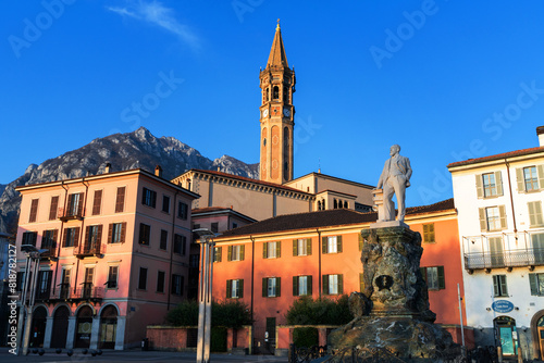Town square with statue, colorful buildings, and clock tower against mountain backdrop