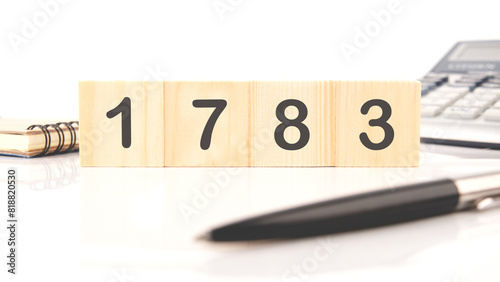The number 1783 written on wooden cubes in a composition with a calculator, a pen on a white background