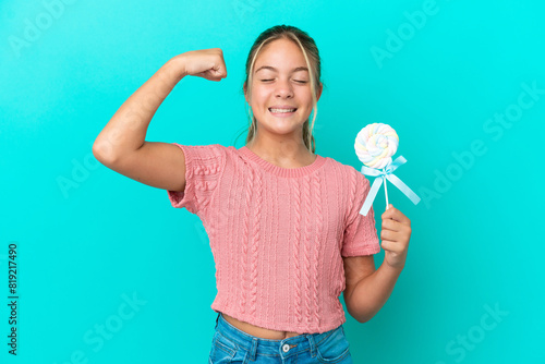 Little Caucasian girl holding a lollipop isolated on blue background doing strong gesture
