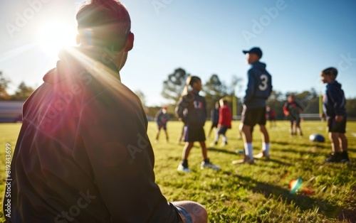 A coach watches young players on a sunny football field.