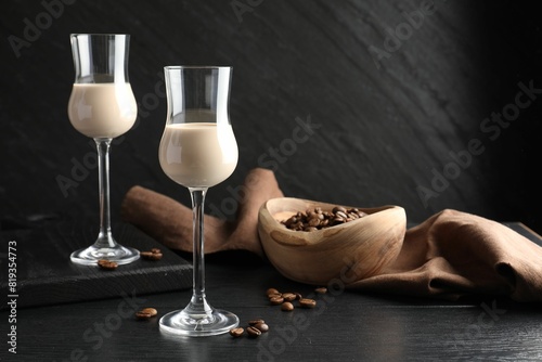 Coffee cream liqueur in glasses and beans on black wooden table