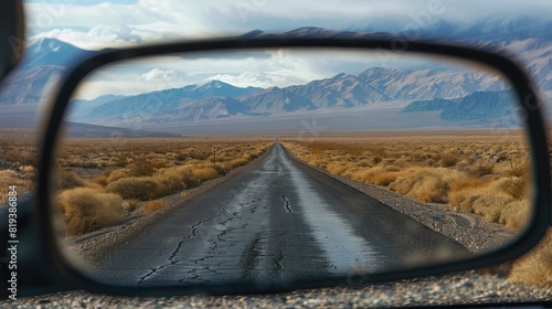 Close-up of a rearview mirror reflecting a long, open road with mountains in the distance