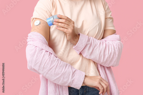 Woman with glucose sensor for measuring blood sugar level and applicator on pink background. Diabetes concept