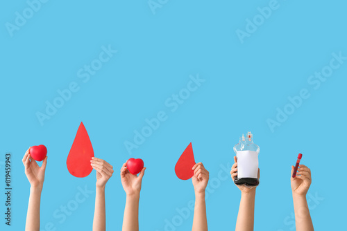 Female hands holding blood pack, test tube, hearts and paper blood drops on blue background. Blood donation concept