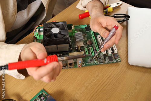 Male technician with soldering iron repairing computer at table in service center, closeup