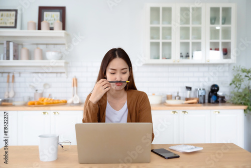 Asian young woman seriously working on computer laptop in house. She thinking find solution problem of work
