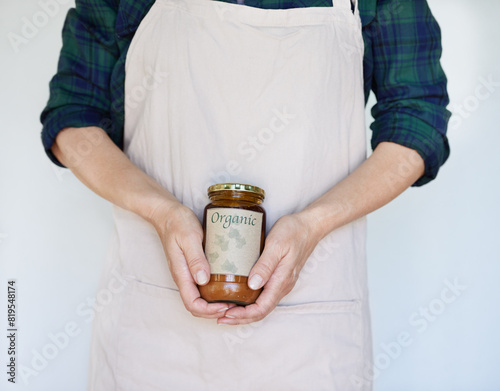 Person, product and hands with organic jam for biodiversity, sustainability and eco friendly in home. Preserver, apron and natural fruit spread for health, quality and wellness on white background