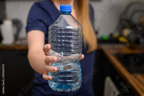 Kobieta trzyma w dłoni butelkę plastikowa z wodą mineralną niegazowaną