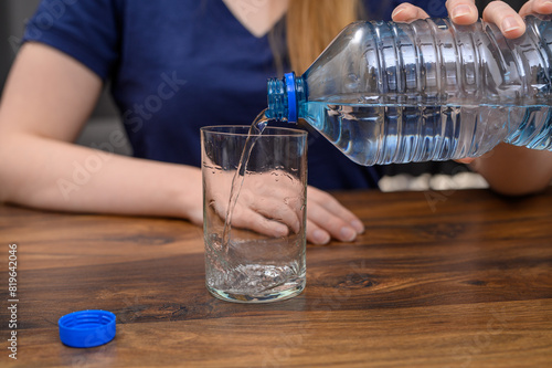 Zmęczona upałem kobieta siedzi przy stole j pije wodę, nalewa wodę źródlaną niegazowaną do szklanki