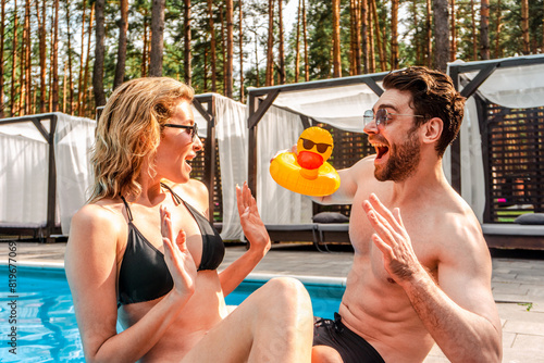 Cheerful young man preparing his female companion for swimming in an outdoor pool. Leisure activity and summer vacation concept