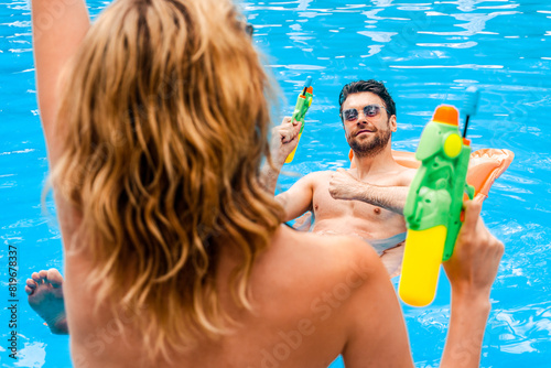 Male and a female looking at each other before playing an outdoor game with water pistols at the poolside. Leisure activity concept