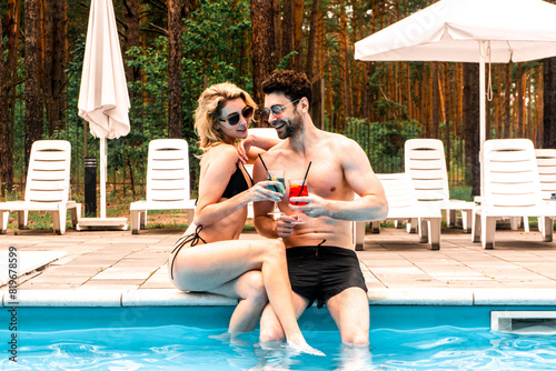 Young happy couple enjoying each other company at the poolside in the recreation area. Rest and relaxation concept