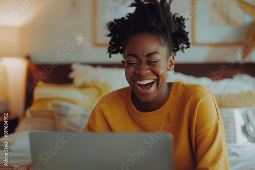 A young woman laughing at something on her laptop screen capturing a moment of leisure and enjoyment at home