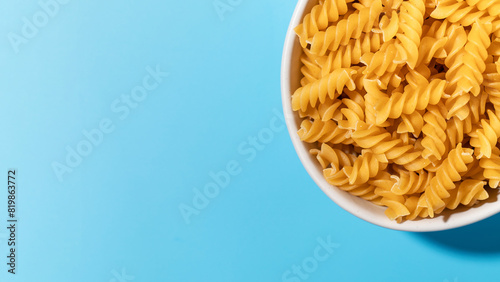 Uncooked fusilli pasta spirals in a white bowl on a blue background. Copy space