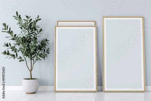 Three blank horizontal poster frames in a Scandinavian style living room with a light blue and white color scheme. Frames are aligned vertically beside a sleek indoor plant.