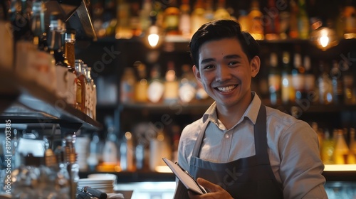 . A friendly waiter, wearing his work uniform, poses with a bright smile as he makes notes in his notepad, the energetic ambiance of the bar counter enhancing the photo. 