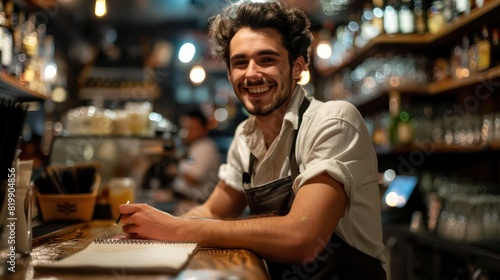 A cheerful young waiter, wearing his work uniform, smiles warmly as he takes notes in his notepad, the bustling activity of the bar counter adding energy to the scene. 