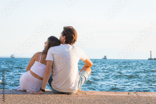 Young couple sitting by the sea in Thessaloniki during a sunny summer day.