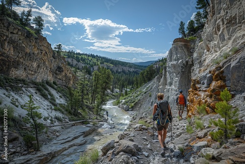 Hikers traverse a rocky path in Yellowstone, awe and adventure on their faces as they marvel at geysers and lush forests, captured in breathtaking ultra-wide views.