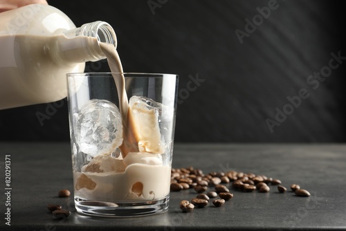 Pouring coffee cream liqueur into glass at grey table, closeup. Space for text